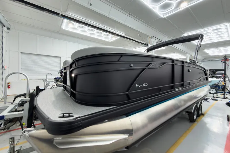 Slide: The Image of 2026 Godfrey Monaco 25' Tritoon in showroom, featuring sleek black design and modern amenities. - 5