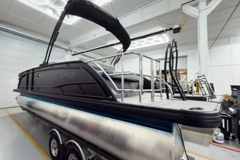 Slide: The Image of 2026 Godfrey Monaco 25' Tritoon in showroom, featuring sleek design and modern amenities. - 6