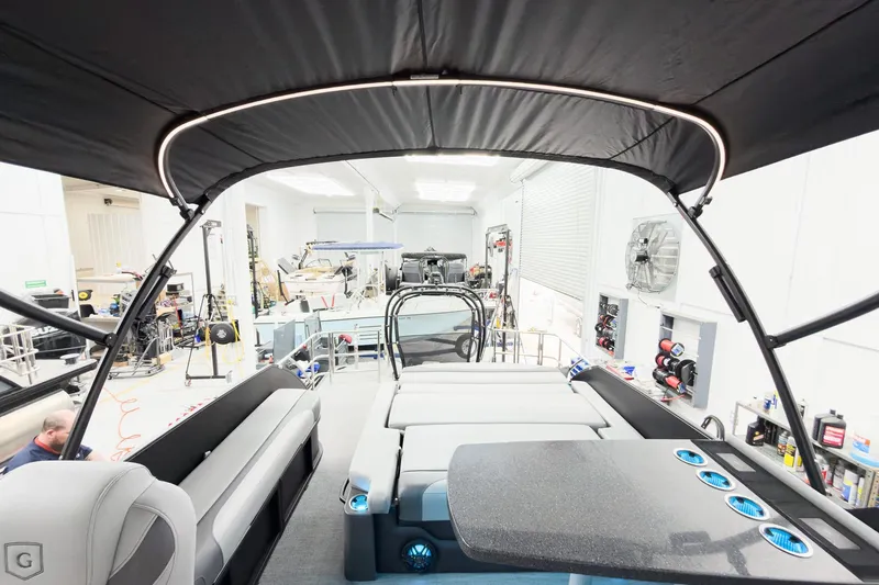 Slide: The Image of 2026 Godfrey Monaco 25' Tritoon interior with mid-table flip lounge in a workshop setting. - 60