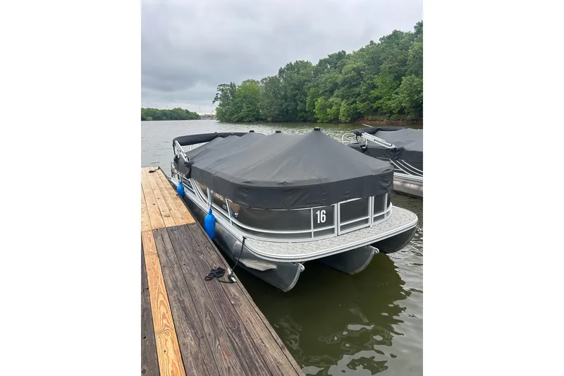 The Image of Covered 2025 Southbay 224RSLE275 pontoon boat docked on a serene lake. - 1