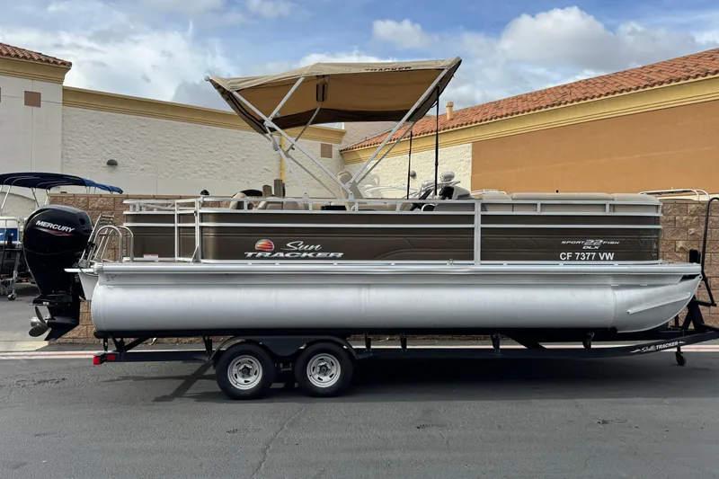 The Image of 2024 Sun Tracker SportFish 22 DLX pontoon boat with canopy, parked on a trailer. - 0