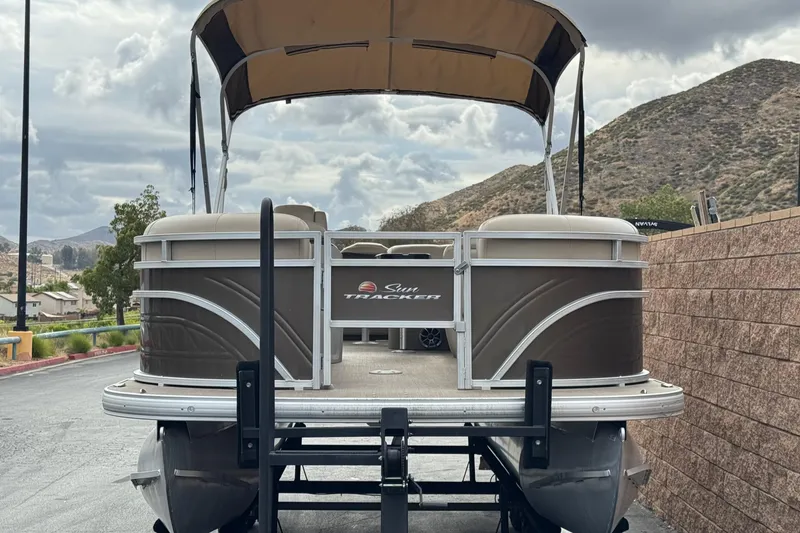 Slide: The Image of 2024 Sun Tracker SportFish 22 DLX pontoon boat on trailer, scenic mountain backdrop. - 2