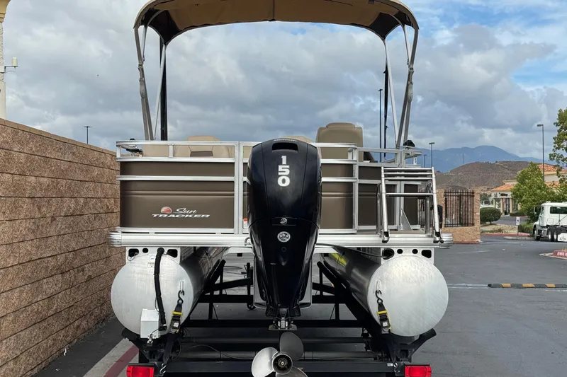 Slide: The Image of 2024 Sun Tracker SportFish 22 DLX pontoon boat with 150 HP engine, parked outdoors. - 4