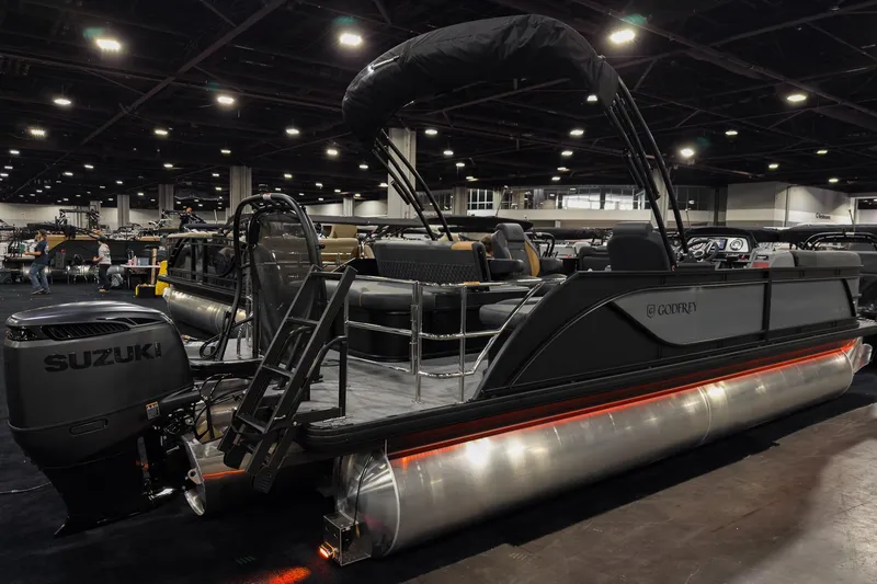 Slide: The Image of 2026 Godfrey Sweetwater 22' Tritoon boat with Suzuki engine at indoor exhibition. - 2