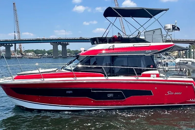 Slide: The Image of 2024 Jeanneau NC Weekender 1095 Fly, red and black, docked near a bridge on a sunny day. - 3