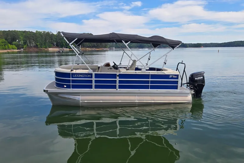 Slide: The Image of 2022 Lexington 320 pontoon boat on a serene lake with a Suzuki outboard motor. - 11