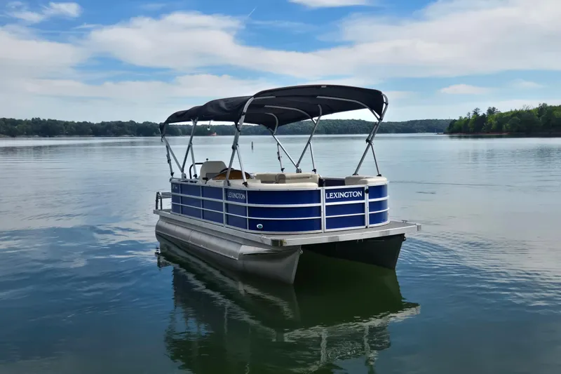 Slide: The Image of 2022 Lexington 320 pontoon boat on a serene lake under a blue sky. - 6