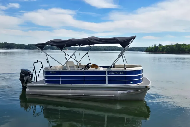 Slide: The Image of 2022 Lexington 320 pontoon boat on a serene lake with blue skies. - 7