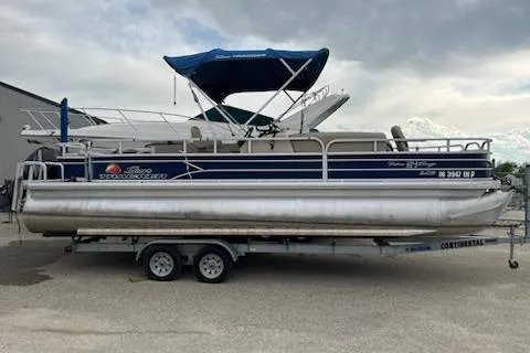 The Image of 2016 Sun Tracker Fishin' Barge 24 XP3 pontoon boat on trailer, blue canopy, parked outdoors. - 0