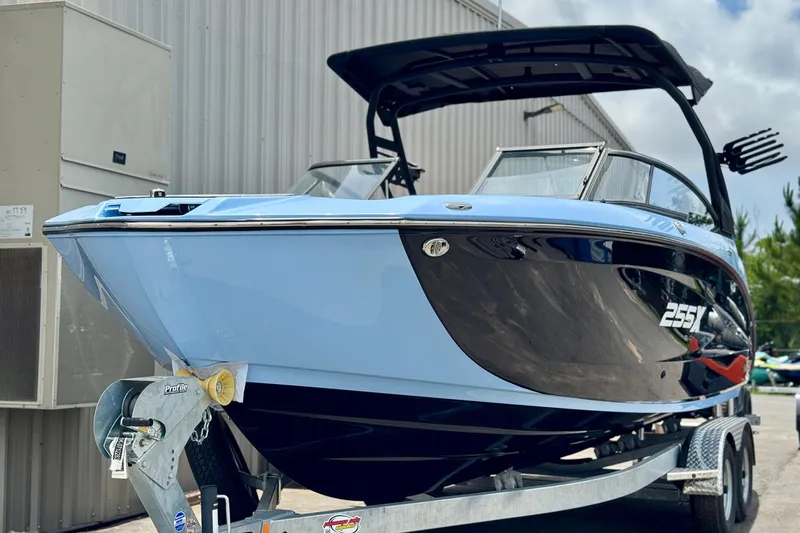 Slide: The Image of 2025 Yamaha Boats 255XD on trailer, sleek design, blue and black exterior, parked outdoors. - 2