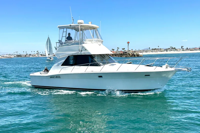 Slide: The Image of 1999 Riviera 3600 Sport Yacht cruising on clear blue waters near a coastal area. - 2