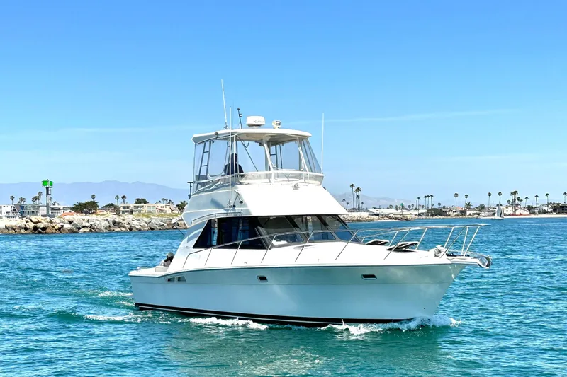 Slide: The Image of 1999 Riviera 3600 Sport Yacht cruising on clear blue waters near a coastal town. - 3