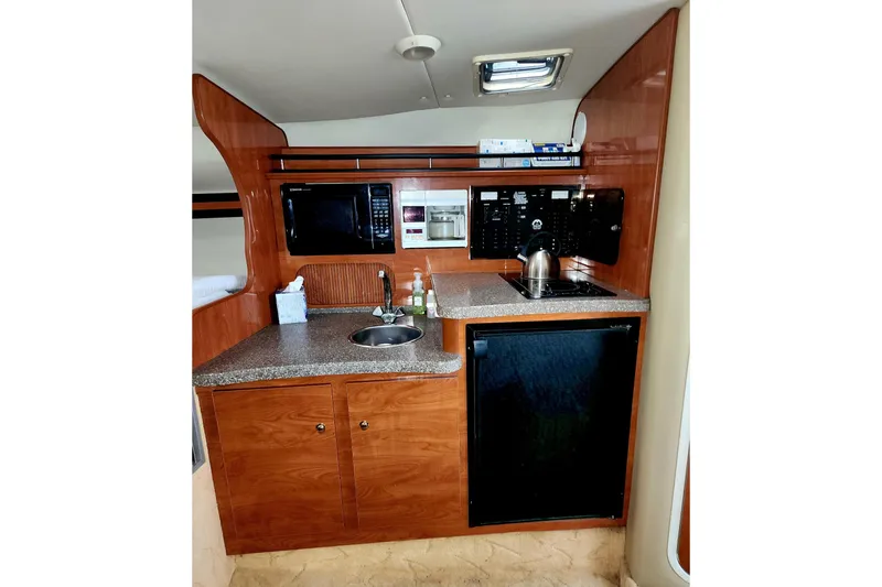 Slide: The Image of 2005 Rinker Fiesta Vee 320 boat kitchen with wood cabinetry, sink, microwave, and mini-fridge. - 5