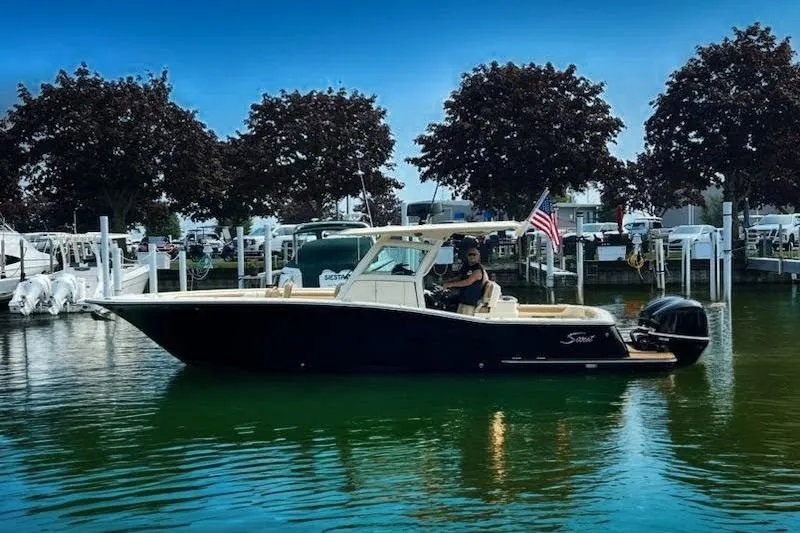 The Image of 2017 Scout 320 LXF boat on calm water near a marina, with trees in the background. - 0