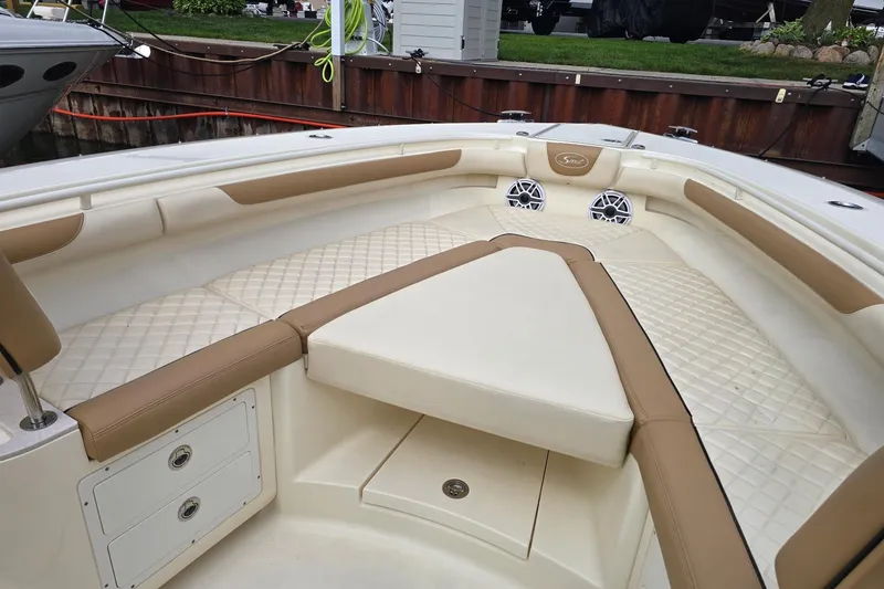 Slide: The Image of 2017 Scout 320 LXF boat interior with tan and white seating, docked by wooden pier. - 19
