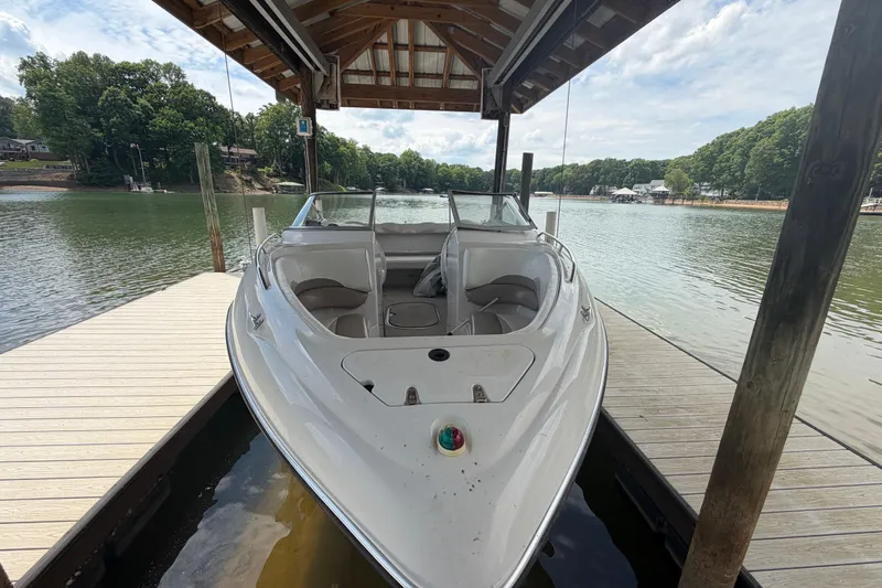 Slide: The Image of 1998 Four Winns 220 Horizon boat docked under a wooden canopy on a serene lake. - 13