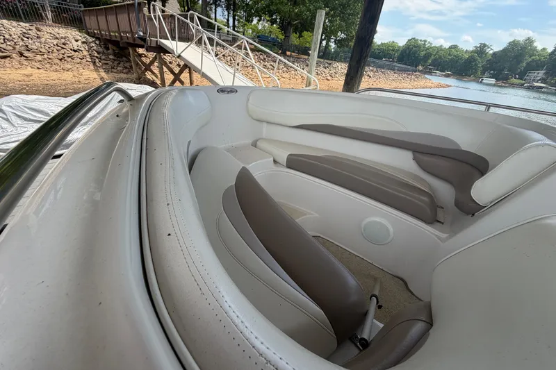 Slide: The Image of 1998 Four Winns 220 Horizon boat interior with white and brown seating near a lakeside dock. - 14