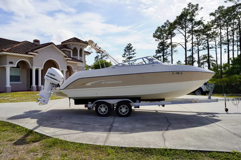 Slide: The Image of 2001 Stingray 240 LS boat on trailer, parked in front of a house with trees in the background. - 4