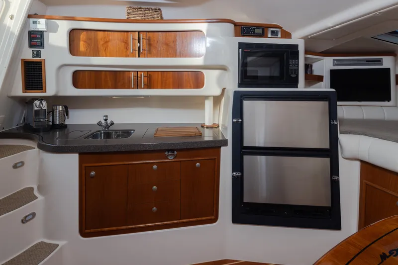 Slide: The Image of 2006 Grady-White Express 360 interior with kitchenette, featuring wood cabinets and stainless steel appliances. - 24