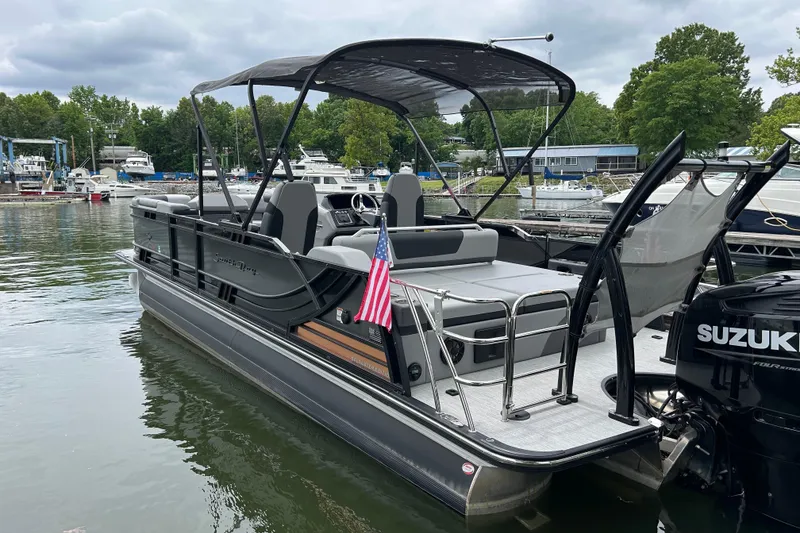 Slide: The Image of 2025 South Bay 525UL393 pontoon boat docked, featuring a Suzuki outboard motor and American flag. - 10