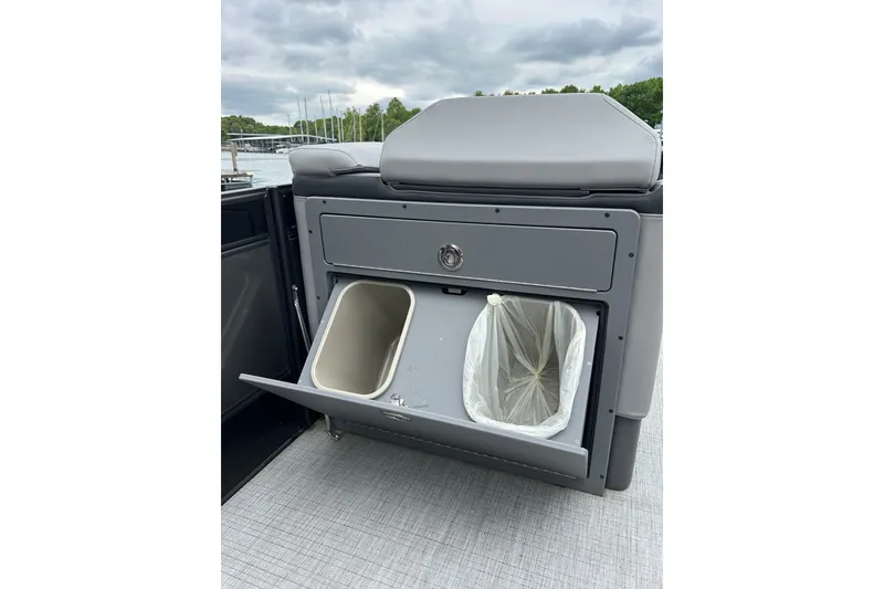 Slide: The Image of 2025 South Bay 525UL393 boat interior with built-in trash compartment, open under cloudy sky. - 37