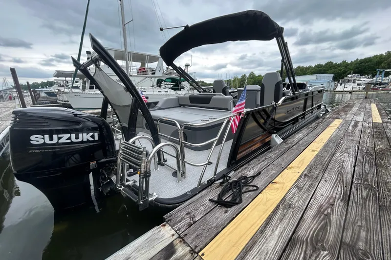 Slide: The Image of 2025 South Bay 525UL393 pontoon boat docked, featuring Suzuki outboard motor and American flag. - 6