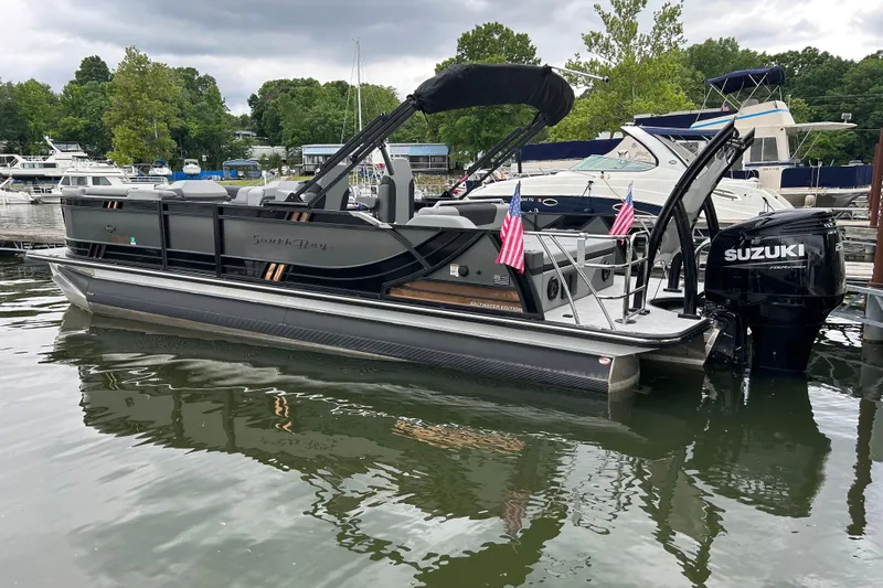 Slide: The Image of 2025 South Bay 525UL393 pontoon boat docked, featuring Suzuki outboard motor and American flags. - 7