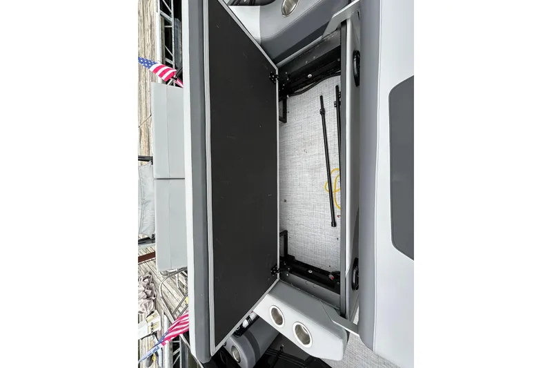 Slide: The Image of Open storage compartment in 2025 South Bay 525UL393 boat, featuring cup holders and American flag. - 31
