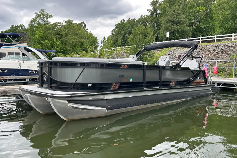 Slide: The Image of 2025 South Bay 525UL393 pontoon boat docked on a lake with lush greenery. - 8