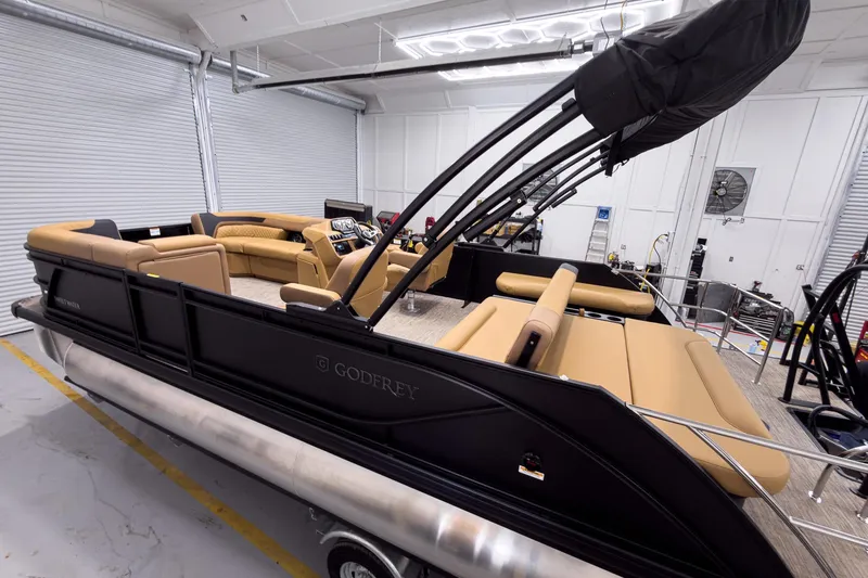 Slide: The Image of 2026 Godfrey Sweetwater 22' Tritoon with tan seating in a garage setting. - 2