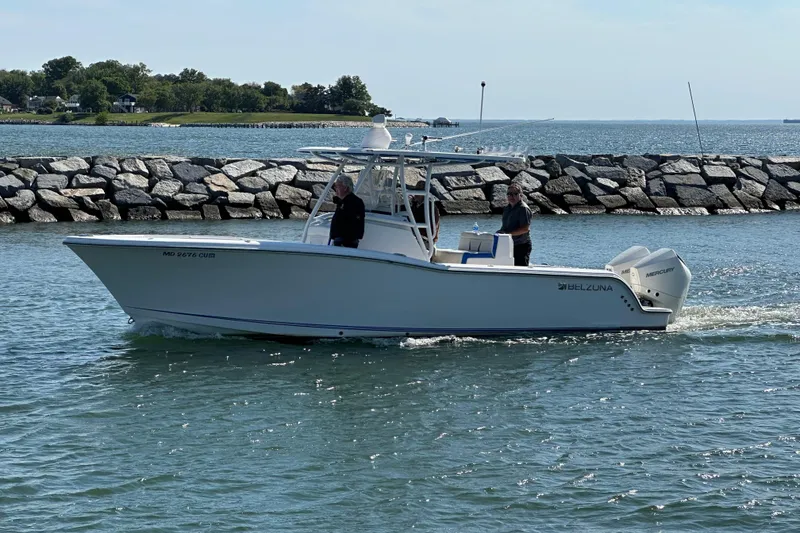 Slide: The Image of 2020 Belzona 27 CC boat cruising near rocky shoreline on a sunny day. - 2