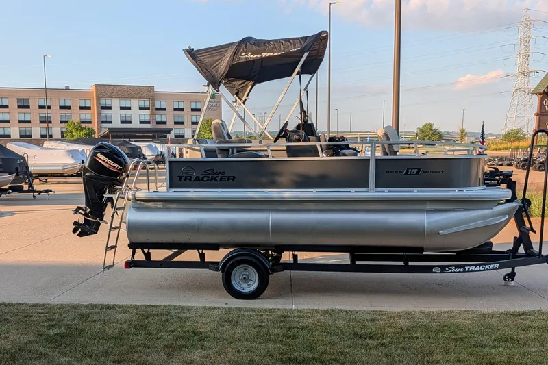Slide: The Image of 2026 Sun Tracker Bass Buggy 16 XL Select pontoon boat on trailer, parked outdoors. - 80