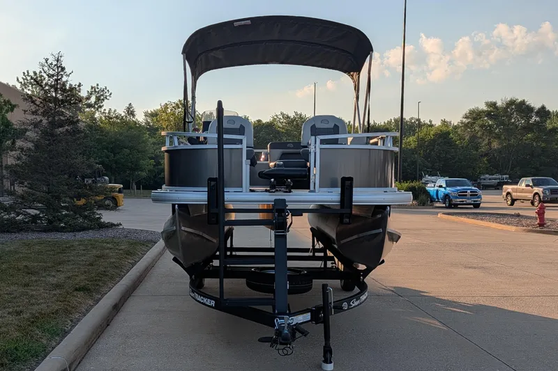 Slide: The Image of 2026 Sun Tracker Bass Buggy 16 XL Select pontoon boat on trailer in parking lot. - 2