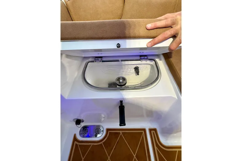 Slide: The Image of 2024 Sea Hunt Ultra 265 SE boat compartment with transparent lid and hand detail. - 18