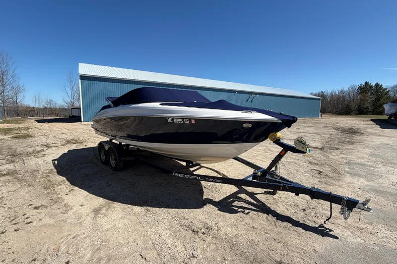 Slide: The Image of 2019 Regal 2300 Bowrider boat on trailer, parked outdoors under clear blue sky. - 4