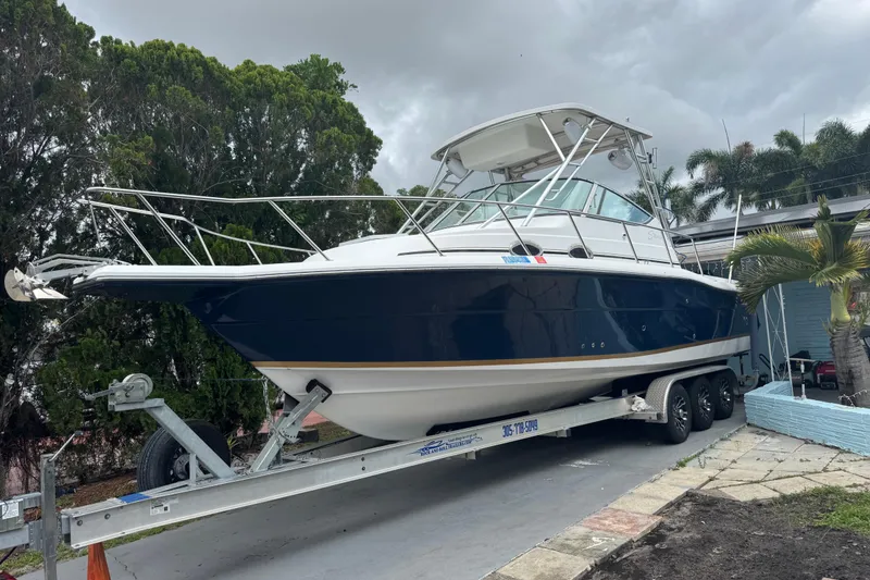 The Image of 2004 Stamas 290 Express boat on trailer, parked outdoors with trees in background. - 0