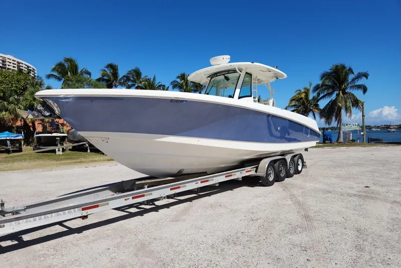 The Image of 2014 Boston Whaler 350 Outrage boat on trailer, parked near palm trees and waterfront. - 0