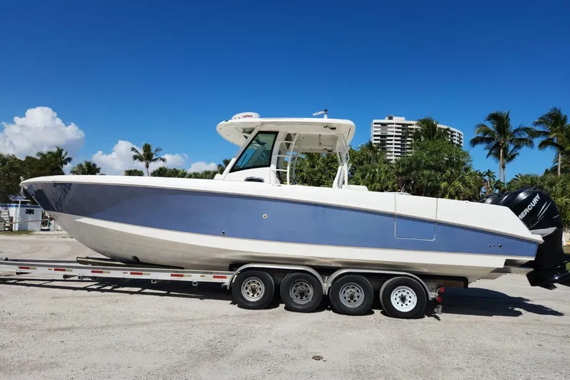 Slide: The Image of 2014 Boston Whaler 350 Outrage boat on trailer, parked outdoors under clear blue sky. - 2