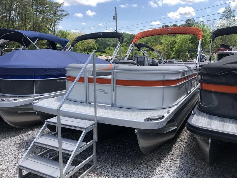 The Image of 2025 Bennington SX L-Bench 22 SXL pontoon boat with orange accents, docked outdoors. - 1