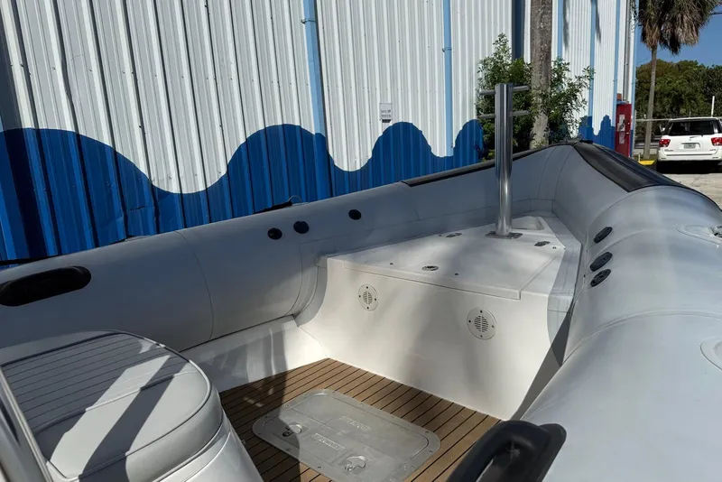 Slide: The Image of 2018 Ribcraft 7.8 boat interior with seating and storage, docked near a blue and white building. - 2