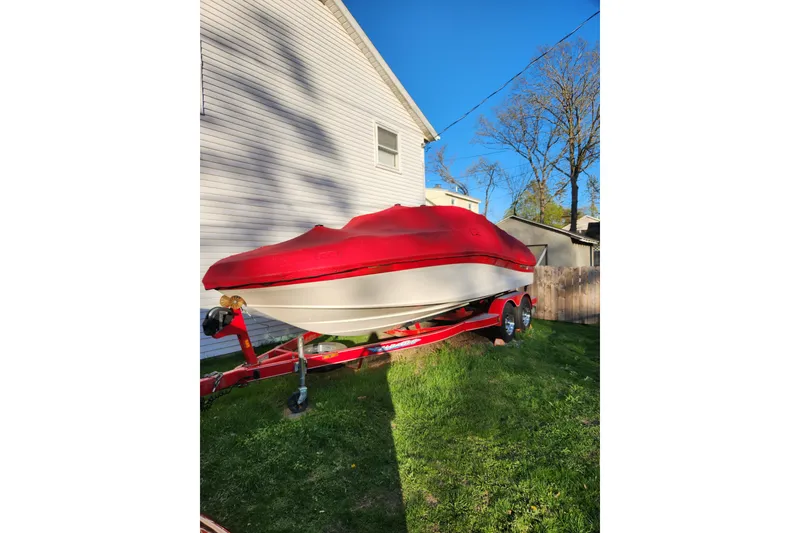 Slide: The Image of 2012 Rinker 216 Captiva Bowrider with red cover on trailer, parked beside house. - 5