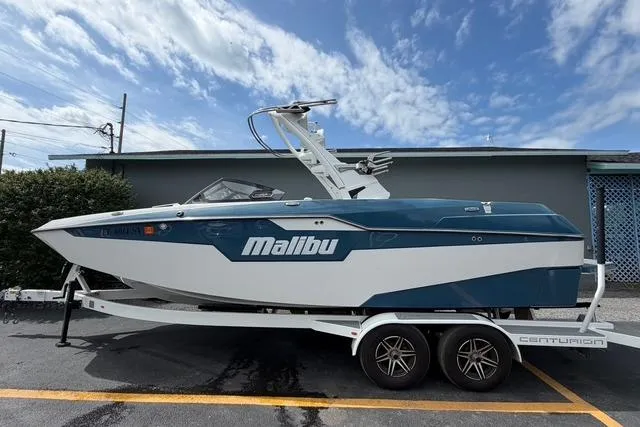 The Image of 2021 Malibu M240 boat on trailer, parked outdoors under a partly cloudy sky. - 1