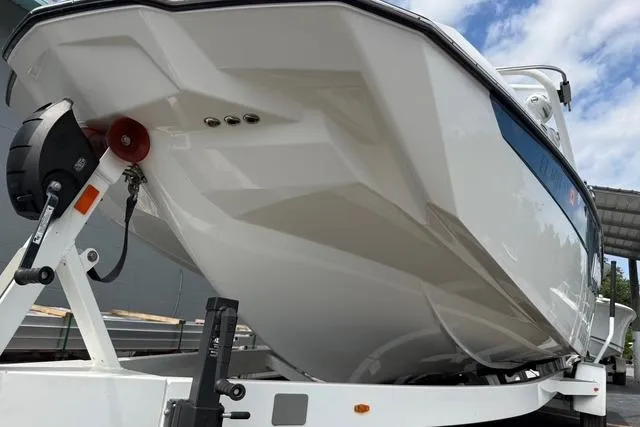 Slide: The Image of 2021 Malibu M240 boat on trailer, showcasing sleek hull design under a partly cloudy sky. - 16