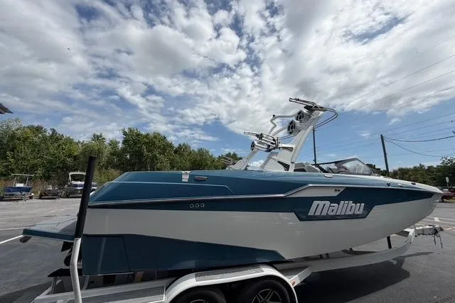Slide: The Image of 2021 Malibu M240 boat on trailer under cloudy sky, side view. - 4