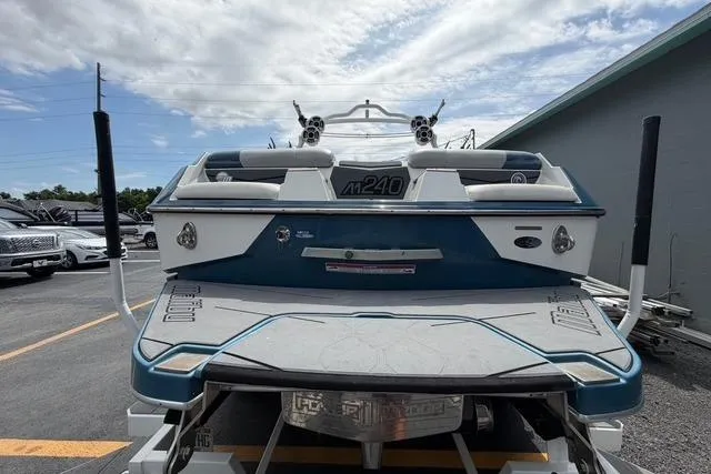 Slide: The Image of 2021 Malibu M240 boat, rear view, parked outdoors under a cloudy sky. - 6
