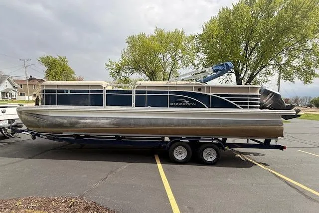 Slide: The Image of 2012 Bennington 2574 GCW pontoon boat on a trailer in a parking lot. - 2