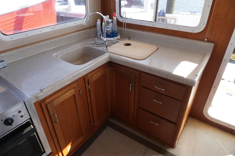 Slide: The Image of 2004 American Tug 34 kitchen with wooden cabinets, sink, and countertop, featuring a window view. - 11