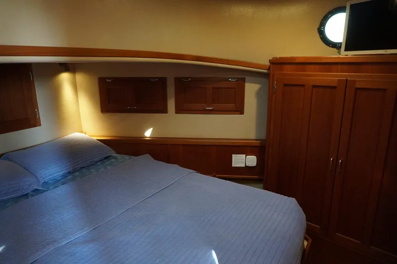 Slide: The Image of Cozy cabin interior of 2004 American Tug 34 with bed, wooden cabinets, and porthole window. - 28