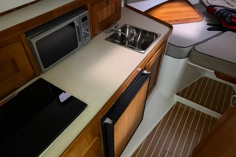 Slide: The Image of 2007 Hunt Yachts Surfhunter 29 interior with kitchenette, featuring microwave, sink, and wooden cabinetry. - 11