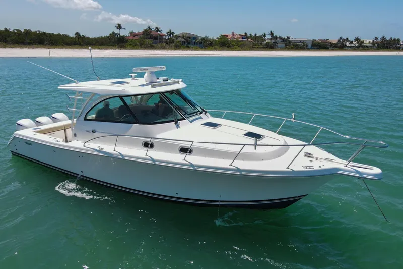 Slide: The Image of 2019 Pursuit OS 385 Offshore boat cruising on clear blue water near a sandy beach. - 43